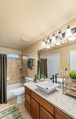 Main Level Common Bathroom Wood-finish vanity with a vessel sink, a light-toned countertop, and an extended mirror
