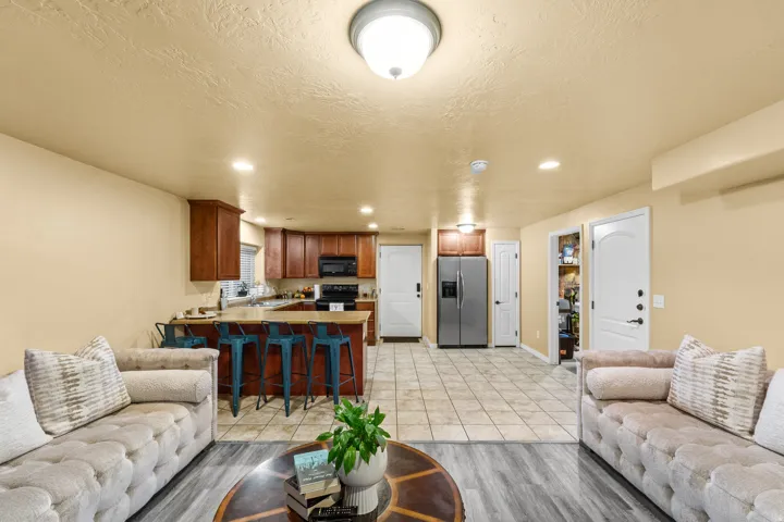 Open-concept living area with wood-finish flooring, recessed lighting, and a kitchen featuring wood cabinetry, a breakfast bar, and stainless steel refrigerator