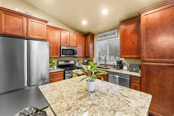 Kitchen featuring wood cabinetry, stainless steel appliances, a center island with a stone-finish countertop, and recessed lighting