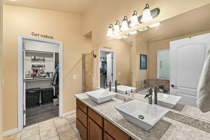 Master Bathroom Vanity with dual vessel sinks, wall-mounted light fixture, and large mirror