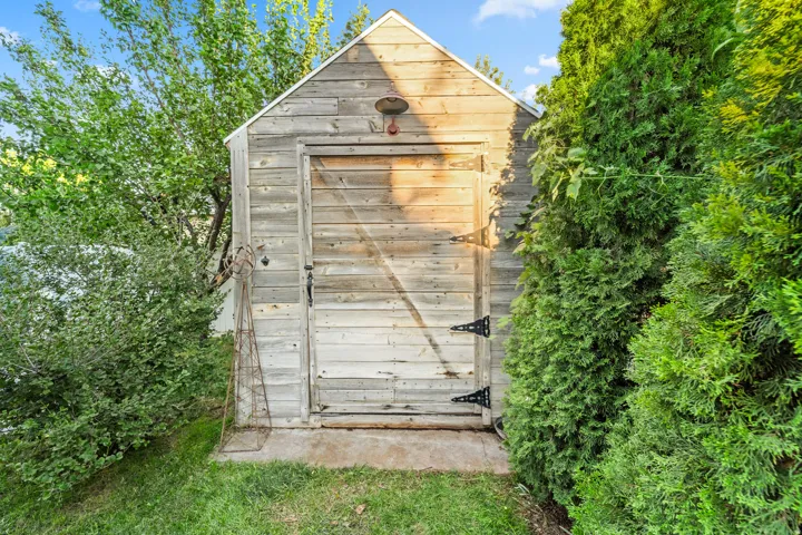 Wood-sided storage shed with a gabled roof and a wooden door featuring black strap hinges