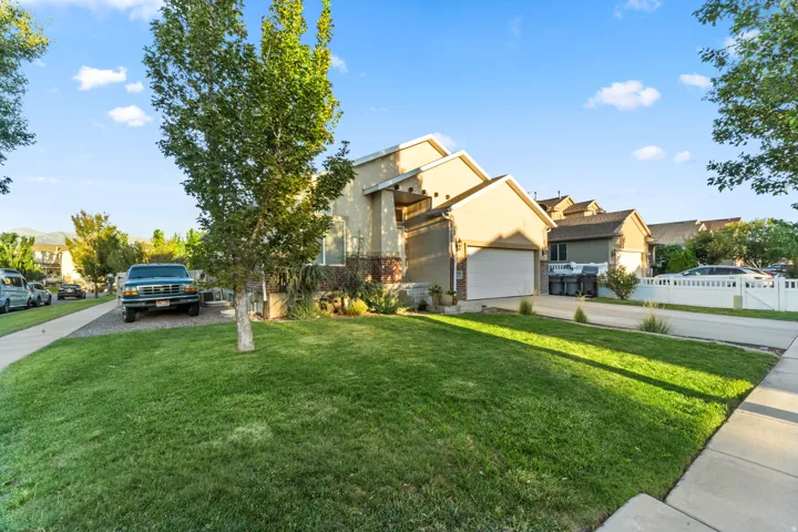 Corner Lot View of Property. Exterior featuring a manicured lawn, established trees, and a two-car garage