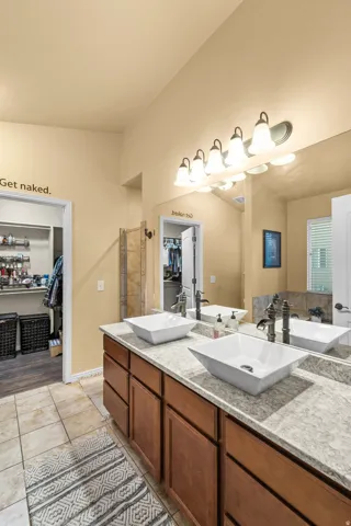 Master Bathroom Dual vessel sinks set atop an extended vanity with wood-finish cabinetry, a large wall-mounted mirror, and tile flooring