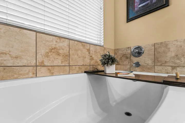 Master Bathroom White built-in bathtub with a tiled surround, chrome fixtures, and a window with blinds