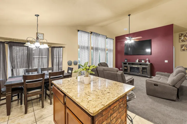 Kitchen island with granite countertop and brick base, tile flooring, vaulted ceiling, ceiling fan, and recessed media console with an integrated electric fireplace