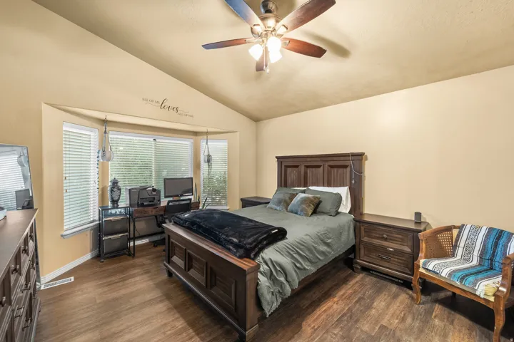 Vaulted ceiling with a ceiling fan, bay window with blinds, wood-finish flooring, and light-toned walls