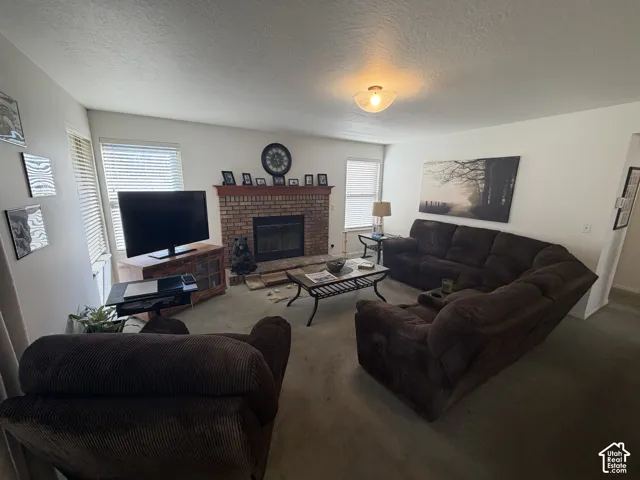 Spacious living room featuring a brick fireplace with mantel display, carpet flooring, dual-pane windows with plantation shutters, and recessed ceiling lighting