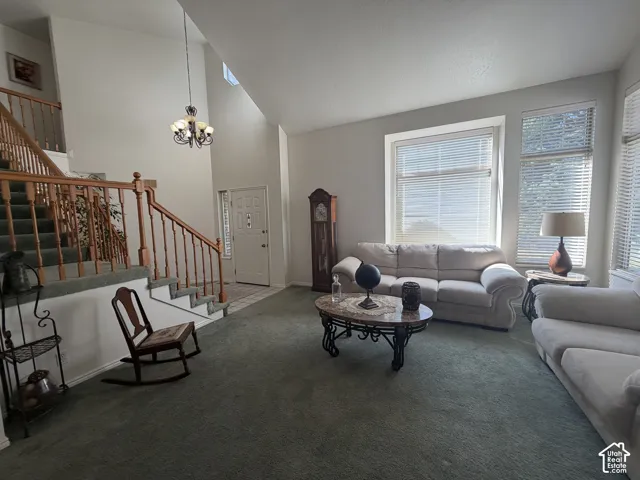Expansive living area featuring vaulted ceilings, a prominent staircase with wood banister, multiple large windows, and a classic chandelier