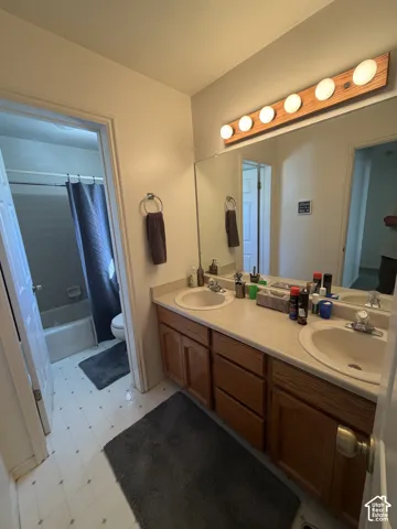 Double vanity with integrated sinks, wood-finish cabinetry, and overhead lighting