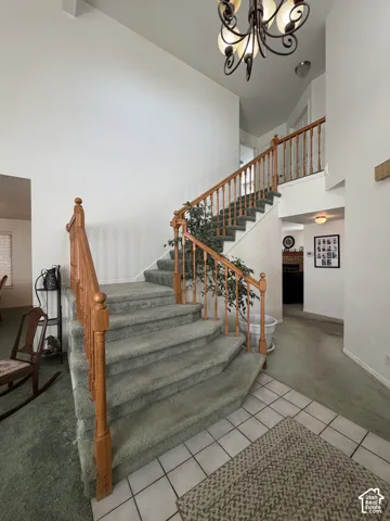 Two-story foyer featuring a grand staircase with wood banisters, wrought iron chandelier, and tile flooring