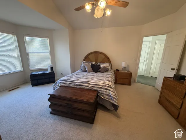 Carpeted room featuring a vaulted ceiling, ceiling fan with light fixture, and two windows with blinds