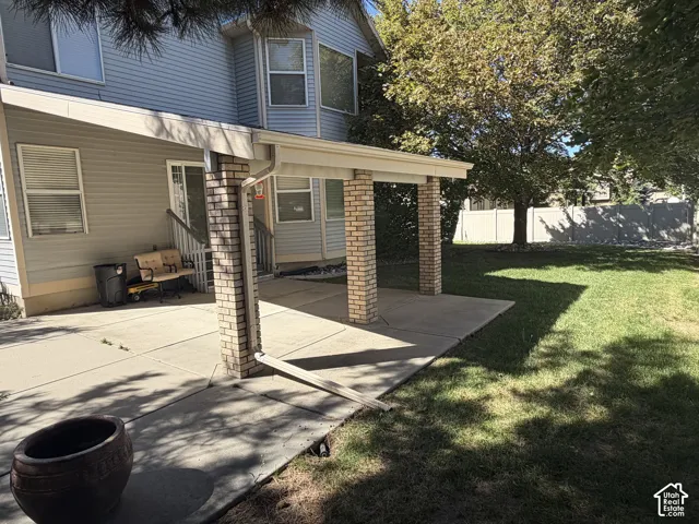 Spacious backyard featuring a covered patio with brick columns, concrete patio, sliding glass door access, and mature trees
