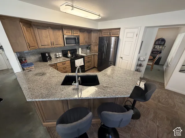 Kitchen featuring wood cabinetry, stainless steel microwave, black appliances, and a peninsula with a dark basin sink and light-toned countertop