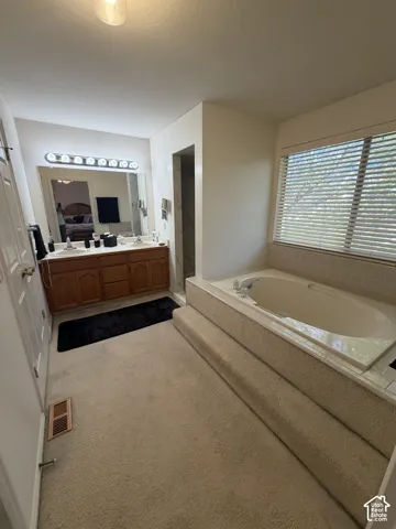 Dual vanity with wood-finish cabinetry, built-in soaking tub with tiled surround, and separate shower enclosure