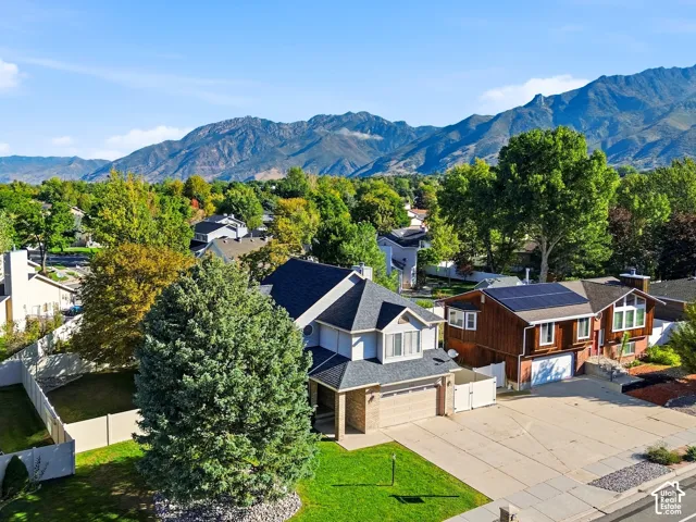 Expansive mountain backdrop, lush green landscaping, mature trees, and a residential street