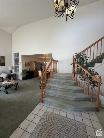 Vaulted ceilings with a chandelier, wood staircase with carpeted treads, and tiled entry flooring