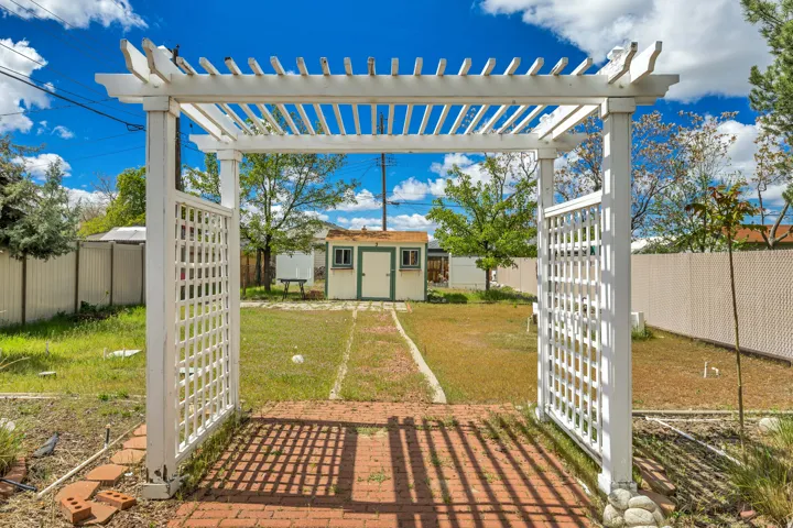 White pergola with lattice accents over a brick paver pathway leading to a detached shed