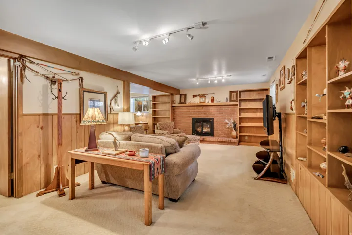 Spacious living area featuring track lighting, a brick fireplace, wood paneling, and extensive built-in shelving