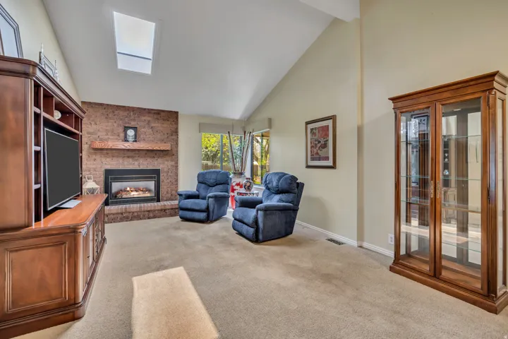 Vaulted ceiling with skylight, brick-faced fireplace with wood mantel, and large window
