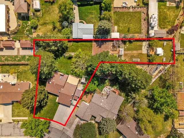 Aerial view of the property featuring a substantial lot, mature trees, and a residential structure with an attached driveway