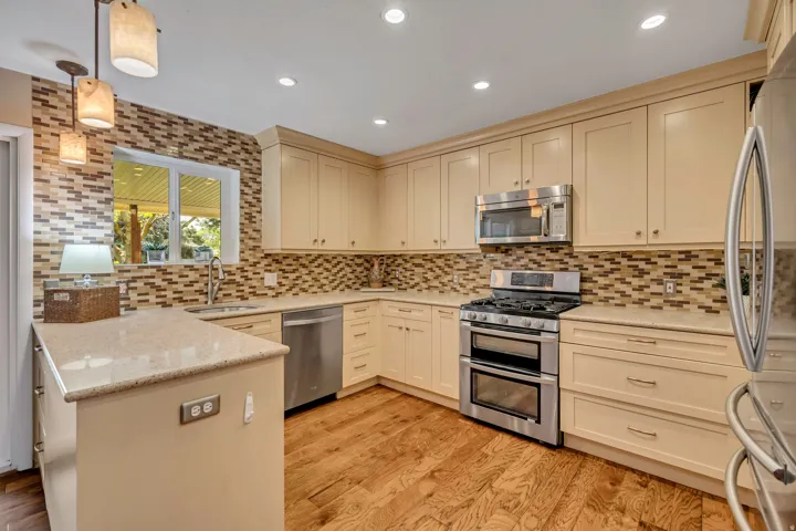Kitchen featuring wood-finish flooring, recessed lighting, light-toned cabinetry, stainless steel appliances, and a mosaic tile backsplash