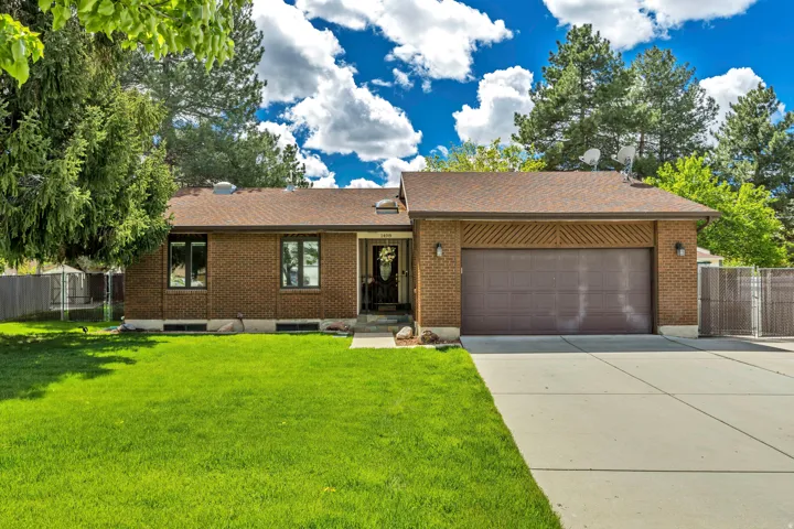 Brick exterior with an attached two-car garage, concrete driveway, and mature landscaping