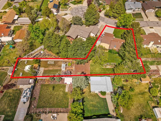 Expansive property featuring a multi-level house with a brown shingle roof, a generously sized grassy yard, mature trees, and an established garden area