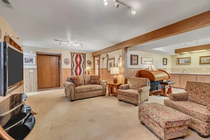 Carpeted recreation room featuring wood paneling, exposed wooden beams, and track lighting