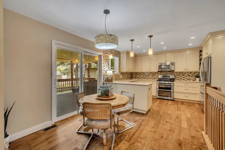 Wood-finish flooring throughout, kitchen with light-toned cabinetry, stainless steel appliances, and a mosaic tile backsplash