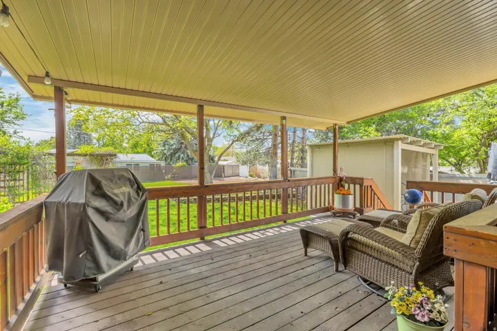 Covered wood-finish deck with railing, supported by timber posts, overlooking a grass yard