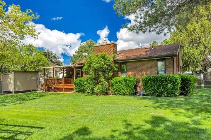 Expansive green lawn, wood deck, brick exterior, storage shed, and mature perimeter landscaping