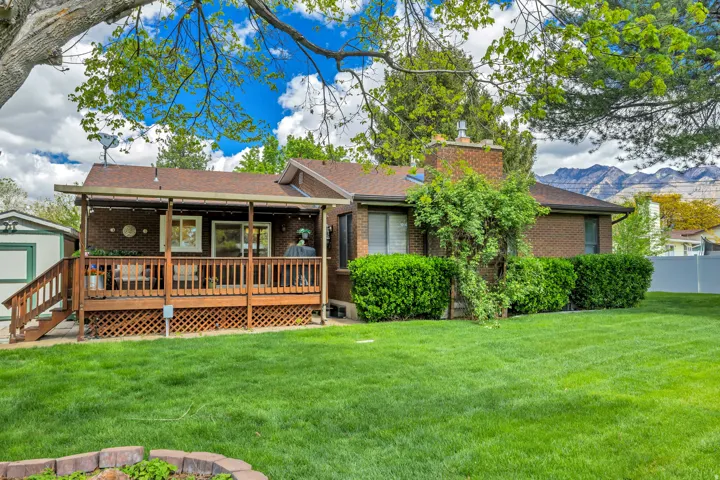 Expansive backyard featuring a manicured lawn, brick exterior, and a covered wood deck with railing and stairs