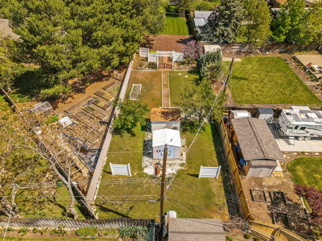 Expansive property featuring mature trees, multiple raised garden beds, a dedicated greenhouse structure, and a detached shed