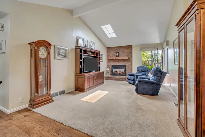 Vaulted ceiling with skylight, brick fireplace with mantel, and carpeting