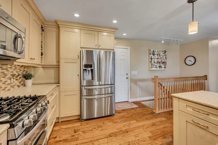 Stainless steel refrigerator, built-in microwave, gas range, wood-finish flooring, and light-toned cabinetry