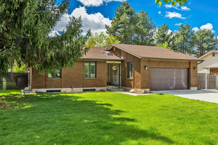 Brick exterior with a brown shingle roof, attached garage, concrete driveway, and a front lawn with mature trees