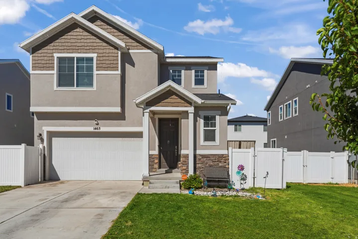 Two-story exterior with a mixed material facade, an attached garage, a paved driveway, a manicured lawn, and white privacy fencing