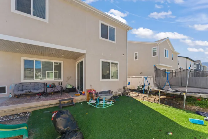 Rear exterior with a covered patio, sliding glass door, multiple windows, and a synthetic turf lawn