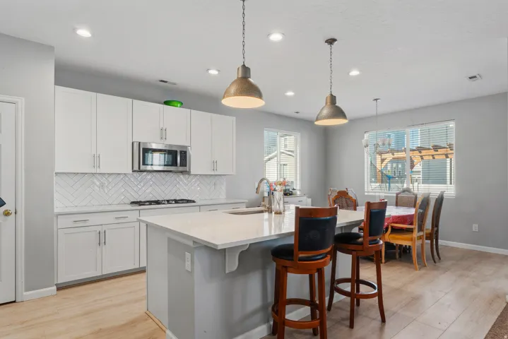 Open-concept kitchen featuring white cabinetry, stainless steel appliances, a tile backsplash, and light wood-finish flooring