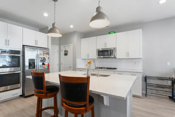 Modern kitchen featuring white cabinetry, stainless steel appliances, a center island with sink, and pendant lighting