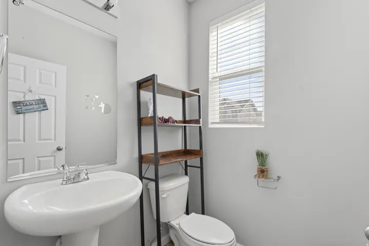 Pedestal sink with chrome faucet, wall-mounted mirror, and natural light from window