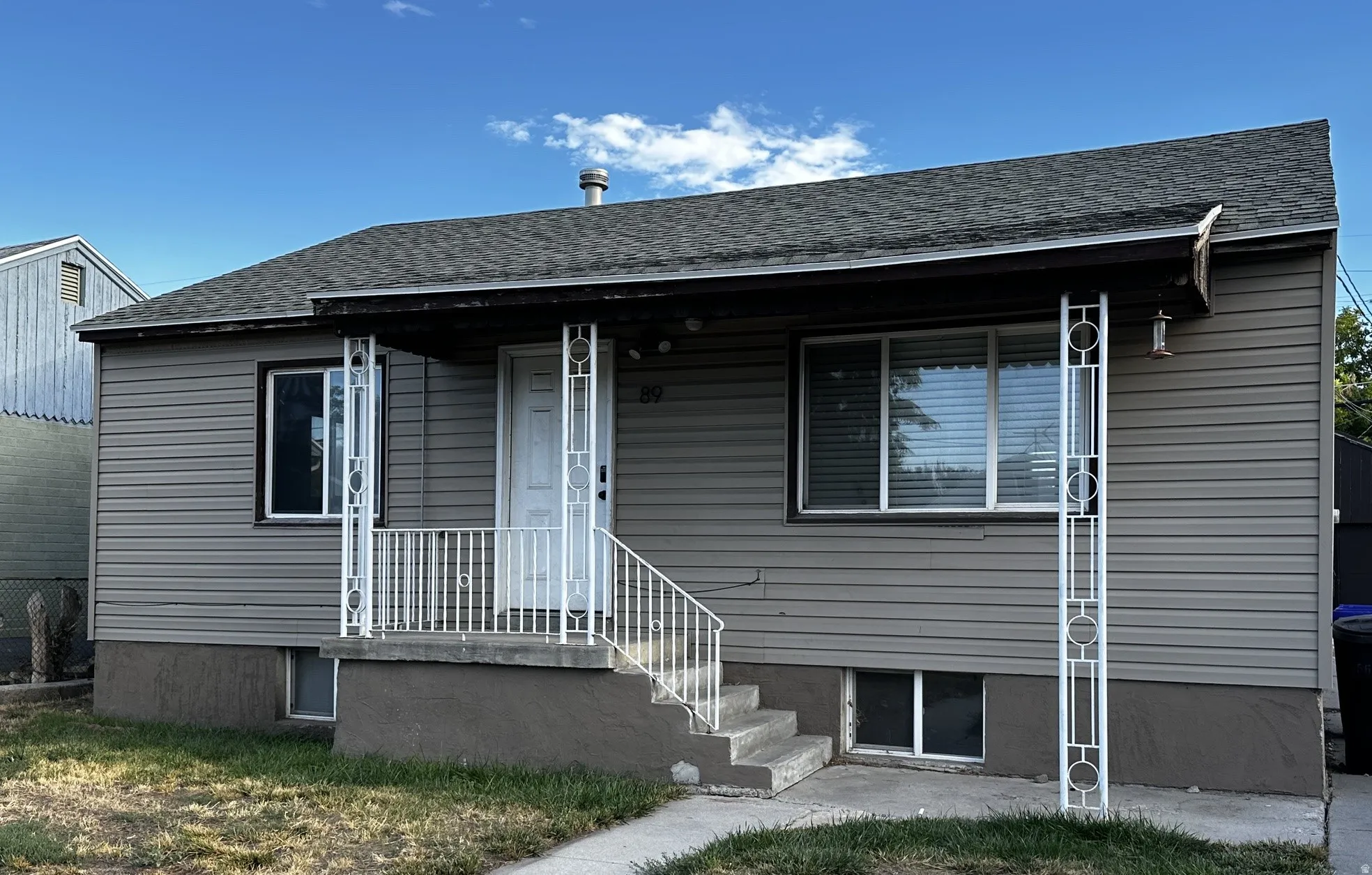 Gray horizontal siding, dark shingle roof, white trim windows, white porch railing, and white decorative porch columns