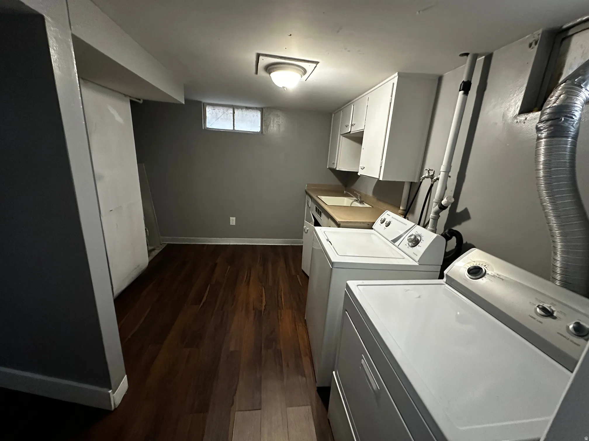 Laundry area featuring wood-finish flooring, white cabinetry, and a utility sink