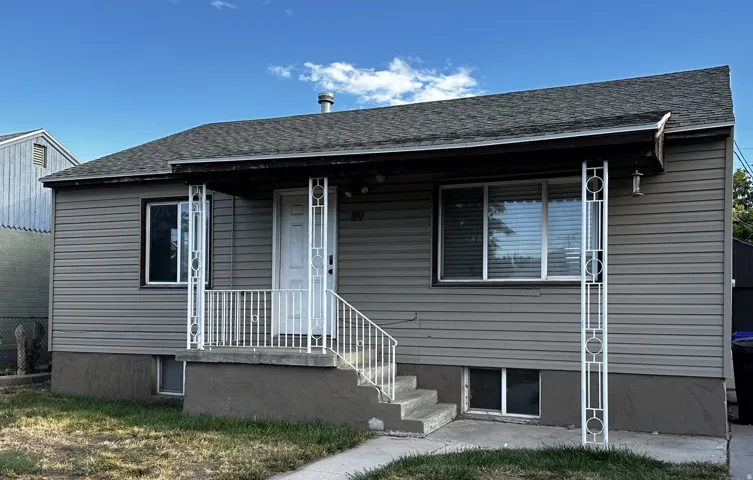Gray horizontal siding, dark shingle roof, white trim windows, white porch railing, and white decorative porch columns