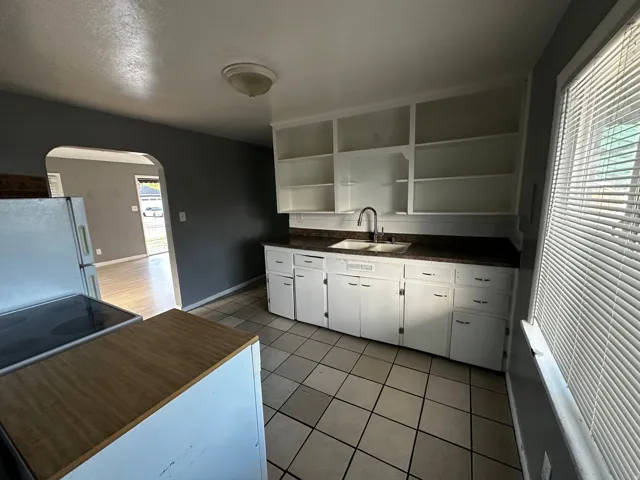 Kitchen featuring white cabinetry, a dual-basin sink with a gooseneck faucet, tiled flooring, and a window with blinds
