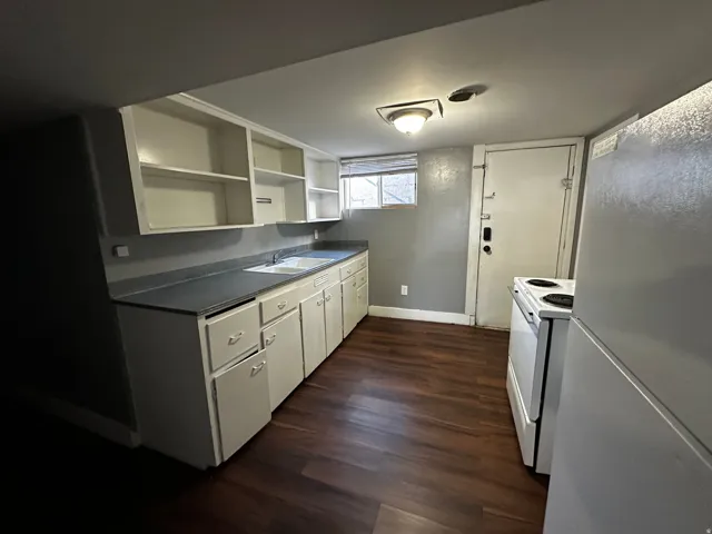 Kitchen featuring wood-finish flooring, white cabinetry, a double basin sink, and white appliances