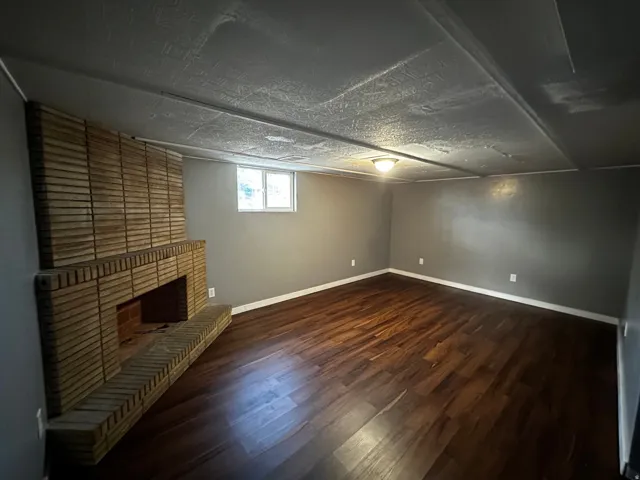 Brick fireplace with hearth, wood-finish flooring, neutral wall paint, ceiling-mounted light fixture, and a window
