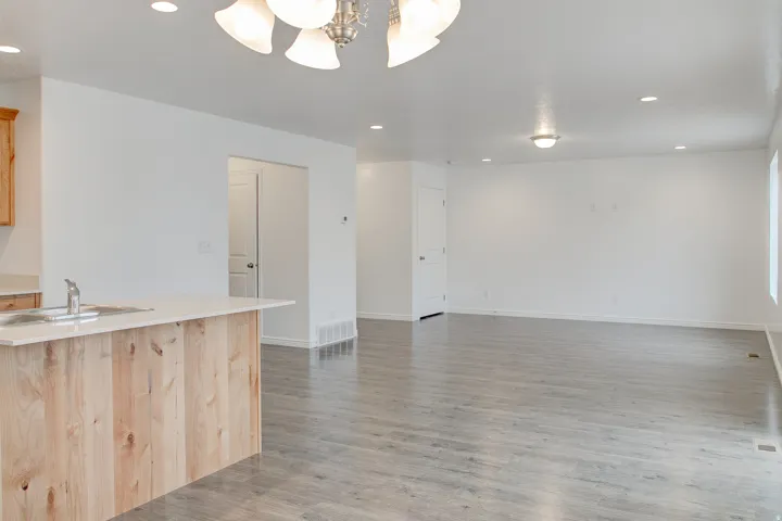 Wood-finish flooring, recessed lighting, and a kitchen island with a built-in sink and light-toned countertop