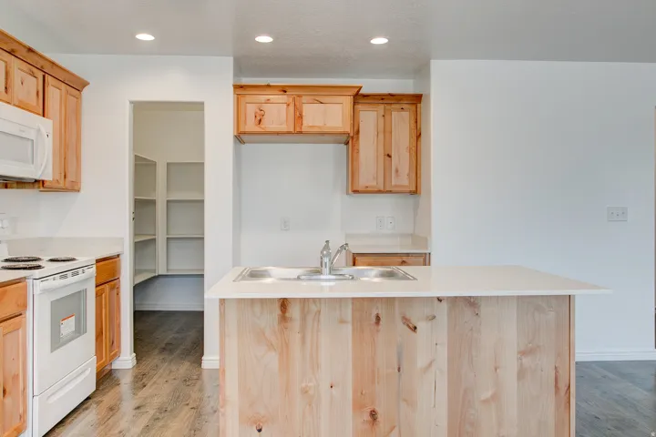Kitchen featuring natural wood-finish cabinetry, white countertops, a dual basin sink, and wood-finish flooring