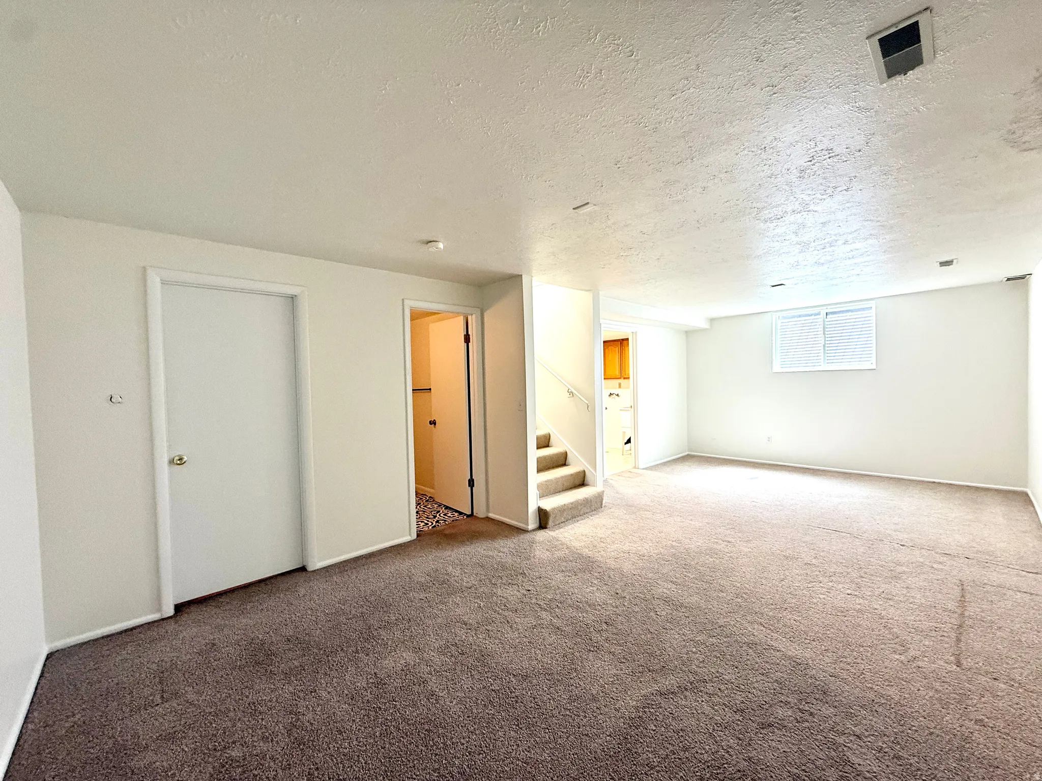 Carpeted room with white walls, a visible staircase, and an interior door